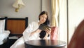 Pretty young woman in bathrobe chatting on tablet computer sitting on chair in hotel room Royalty Free Stock Photo