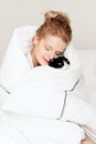 Pretty young woman with black cat in blanket in white bedroom Royalty Free Stock Photo