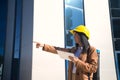 Pretty young woman in brown coat, yellow workman`s helmet and blueprint tube, working with her tablet and pointing with her hand. Royalty Free Stock Photo