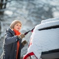 Pretty, young woman cleaning her car from snow after heavy snowstorm Royalty Free Stock Photo