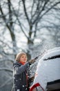 Pretty, young woman cleaning her car from snow after heavy snowstorm Royalty Free Stock Photo
