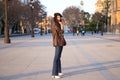 Pretty young woman with curly brown hair wearing a black cap and dressed in a leather jacket, jeans and white boots. She is Royalty Free Stock Photo