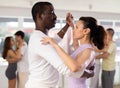 Pretty young woman dancing waltz with african american partner at group of multinational people in ballroom dancing Royalty Free Stock Photo