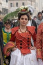 Pretty young woman dressed in carnival dress: red coat, white skirt and small hat with big feathers is posing at the Venice