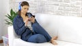 Pretty young woman dressed in jeans  listening music with headphones on white sofa at home Royalty Free Stock Photo