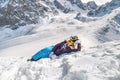 Pretty young woman dressed in winter clothes, glasses and winter funny hat, lying on snow top of the mountain Royalty Free Stock Photo