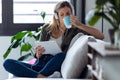 Pretty young woman drinking cup of coffee while listening to music with her digital tablet on sofa at home Royalty Free Stock Photo