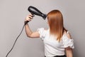 Pretty young woman drying her red hair with dryer over gray background Royalty Free Stock Photo