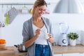 Pretty young woman eating yogurt while standing in the kitchen at home Royalty Free Stock Photo