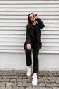 Pretty young woman fashion model in white vintage shoes in stylish black clothing with handbag straightens fashion sunglasses near Royalty Free Stock Photo