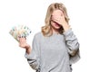 Pretty young woman in grey sweater holding bunch of Euro banknotes, covering her eyes with hand, isolated on white background. Royalty Free Stock Photo