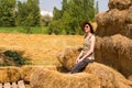 Pretty happy woman with hat sitting on straw bales and getting some rest. Royalty Free Stock Photo