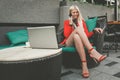 Pretty young woman having cell phone conversation while sitting front open laptop computer Royalty Free Stock Photo