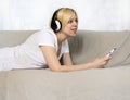 Pretty young woman in headphones lying on sofa listening music or audio book with closed eyes. Joyful beautiful lady enjoying popu Royalty Free Stock Photo