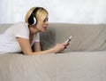 Pretty young woman in headphones lying on sofa listening music or audio book with closed eyes. Joyful beautiful lady enjoying popu Royalty Free Stock Photo