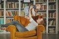 Pretty young woman and her baby child are playing inside room against bookshelves Royalty Free Stock Photo