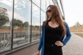 Pretty young woman hipster in sunglasses in a stylish blue knitted cape in a stylish black top with lace in jeans poses Royalty Free Stock Photo