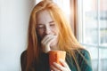 Young woman holding cup with coffee or hot herbal tea and yawning, lack of sleep, tired