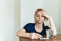 Pretty young woman holding his head and feeling sick. The girl is sitting at the table and looking at pain medication Royalty Free Stock Photo
