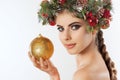 A pretty young woman holds in her hand a golden Christmas ball, on her head a beautiful wreath of spruce with cones and balls. Royalty Free Stock Photo