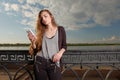 Pretty Young Woman Leaning Back Against Railings on Embankment While Using her Smartphone Reading Sms. Royalty Free Stock Photo