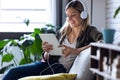 Pretty young woman listening to music with headphones and her digital tablet while sitting on sofa at home Royalty Free Stock Photo