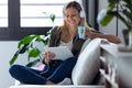 Pretty young woman listening to music with her digital tablet while drinking cup of coffee on sofa at home Royalty Free Stock Photo