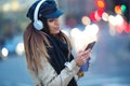 Pretty young woman listening to music with mobile phone while drinking coffee in the street at night Royalty Free Stock Photo