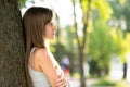 Pretty young woman with long hair standing neat tree trunk in summer