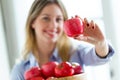 Pretty young woman looking at camera while showing red apple at home