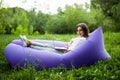 Pretty young woman lying on inflatable sofa lamzac browse in internet on laptop while resting on grass in park Royalty Free Stock Photo