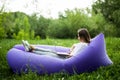 Pretty young woman lying on inflatable sofa lamzac working on laptop while resting on grass in park Royalty Free Stock Photo