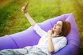 Pretty young woman lying on inflatable sofa lamzac take selfie on phone while resting on grass in park on the sun Royalty Free Stock Photo