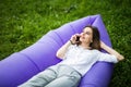 Pretty young woman lying on inflatable sofa lamzac talk on phone while resting on grass in park Royalty Free Stock Photo