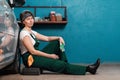 Pretty young woman mechanic is sitting leaning on a car in an auto repair shop. The concept of women's work in male Royalty Free Stock Photo