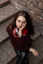Pretty young woman model in a knitted sweater in leather pants with a scarf sits on a stone staircase and looks up at the camera. Royalty Free Stock Photo