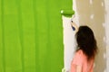 Pretty young woman in pink t-shirt is enthusiastically painting green interior wall with roller in a new home Royalty Free Stock Photo