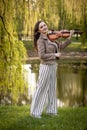 Pretty young woman playing the violin in the park and smiles, Full-length portrait