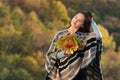 Pretty young woman in a poncho with autumn leaves in hands. Girl touched the hair. Portrait