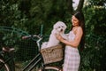 Young woman putting white bichon frise dog in the basket of electric bike Royalty Free Stock Photo