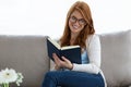 Pretty young woman reading a book while sitting on the sofa at home. Royalty Free Stock Photo
