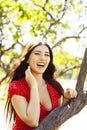 Pretty young woman in red dress smiling cheerful in green park at tree on summer sunny day, lifestyle people concept