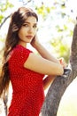 Pretty young woman in red dress smiling cheerful in green park at tree on summer sunny day, lifestyle people concept