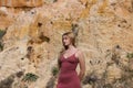 pretty young woman in red summer dress is posing on the cliff. The woman makes different body expressions. In the background rocks Royalty Free Stock Photo