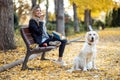 Pretty young woman sending audio messages with her smart phone while sitting on bench with her lovely dog in the park in autumn Royalty Free Stock Photo