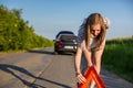 Pretty, young woman setting the safety triangle on the roadside