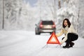 Pretty, young woman setting up a warning triangle and calling for assistance after her car broke down