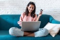 Pretty young woman shopping online with credit card and laptop while sitting on sofa at home Royalty Free Stock Photo
