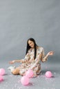 A pretty young woman sits near pink balloons and throws up confetti and smiles and on a gray background Royalty Free Stock Photo