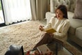 Pretty young woman sitting in cozy living room and making notes to her diary Royalty Free Stock Photo